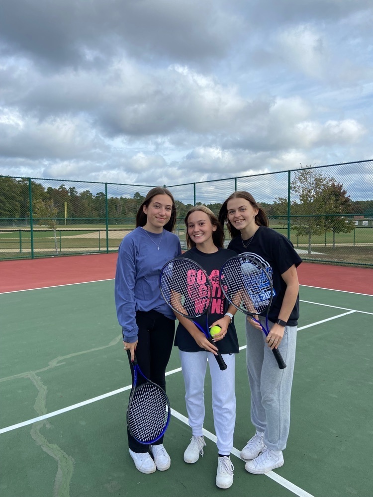 three students holding tennis rackets 